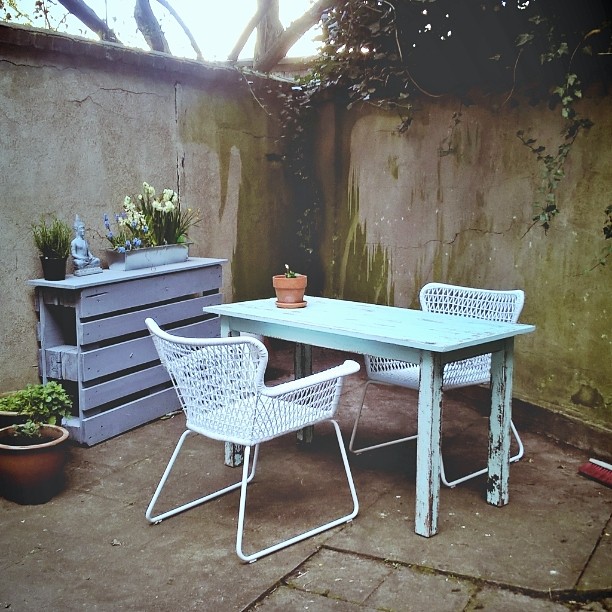 Ein Garten mit Tisch, zwei Stühlen, Konsoltisch und Blumentöpfen