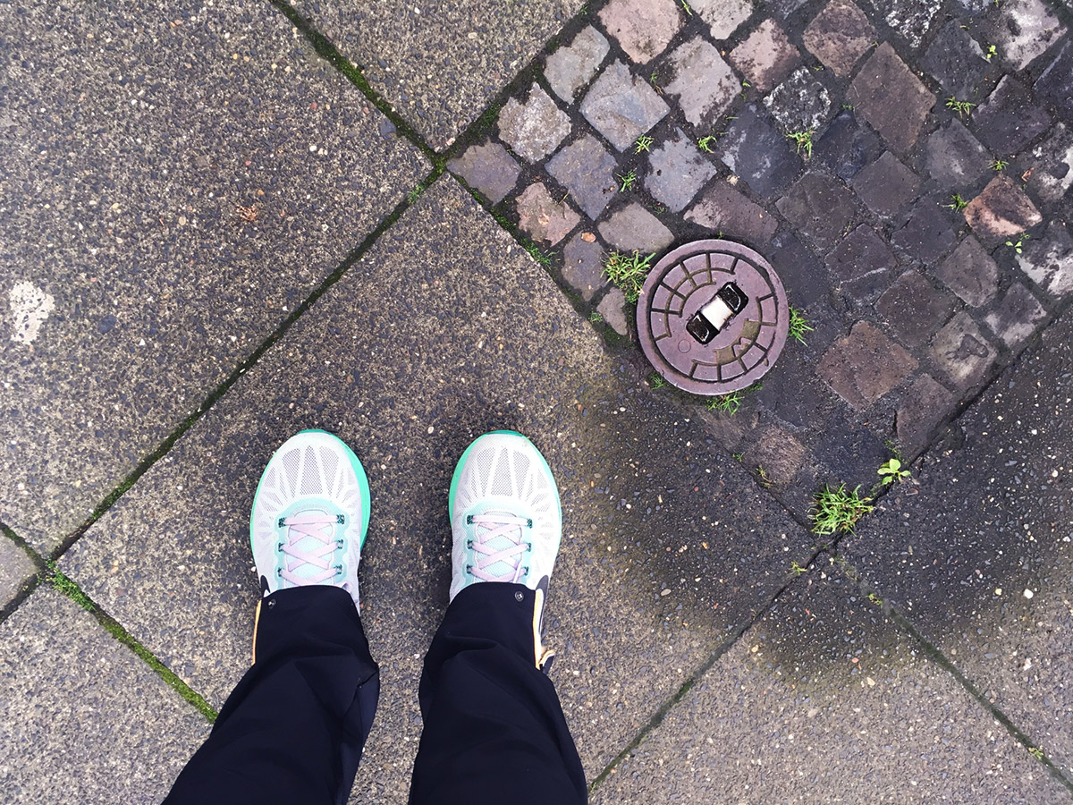 Blick von oben auf Füße in Joggingschuhen, Untergrund ist ein Bürgersteig mit Gehwegplatten