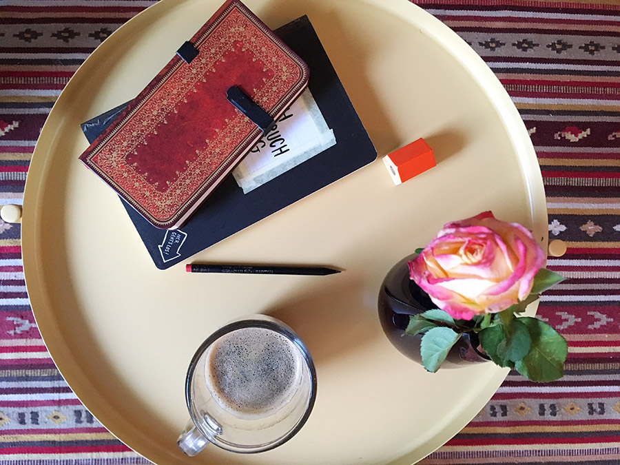 Verschiedene Notizbücher, ein Bleistift, eine Vase mit einer Rose und eine Kaffetasse stehen auf einem Couchtisch