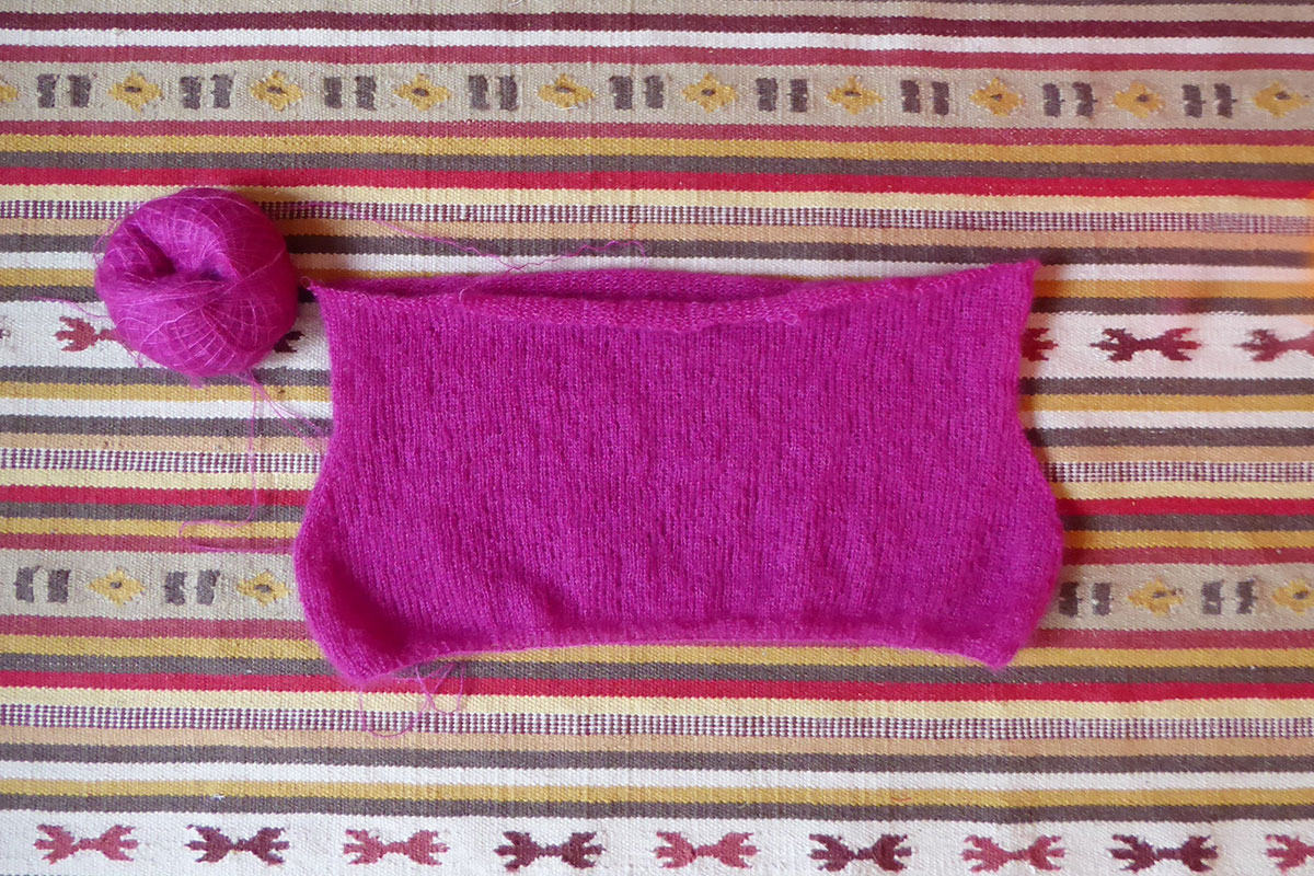 Ein Strickzeug aus pinkfarbener Mohairwolle liegt auf einem Kelimteppich