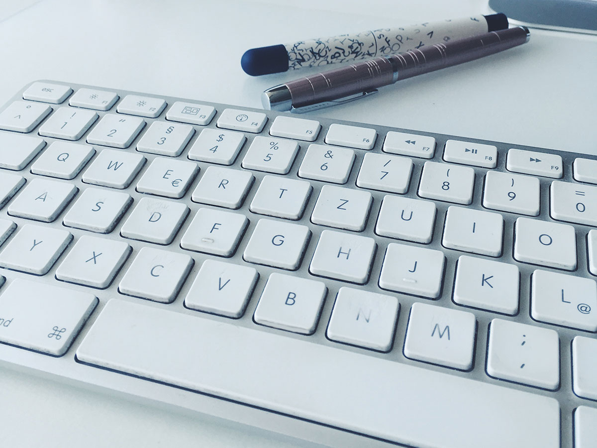 Eine Apple Tastatur dahinter liegen zwei Stifte