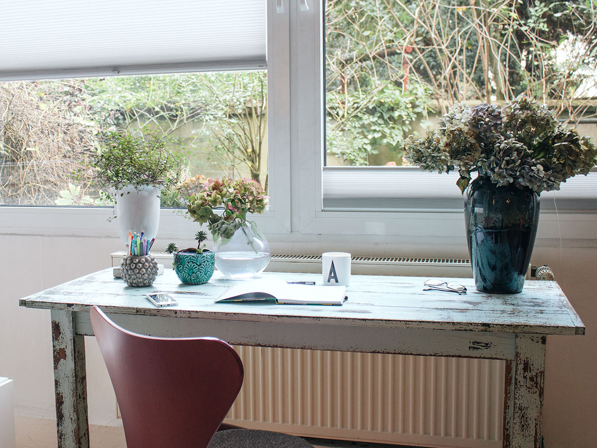Ein Schreibtisch im Shabby-Chic-Look steht vor einem Fenster darauf Vasen in unterschiedlichen Formen