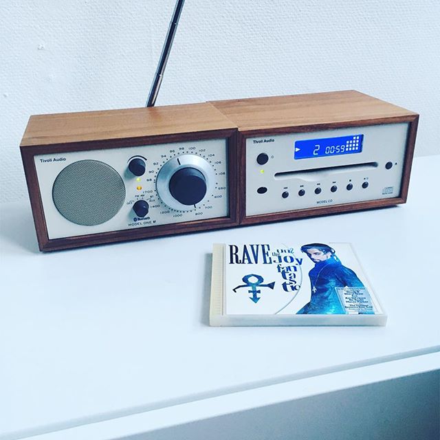 Ein Tivoli Audio Model One und Model TV stehen auf einem weißen Sideboard, davor liegt eine CD von Prince