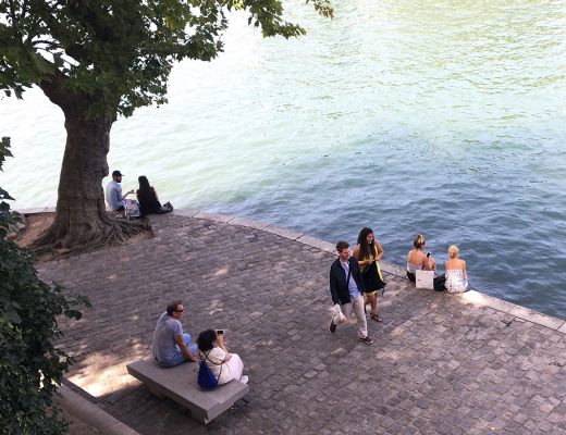 An einem Sommertag: Ein Quai in Paris, Menschen flanieren oder sitzen in der Sonne