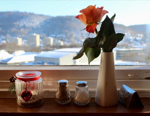 Ein Teelicht, ein Salz- und Pfefferstreuer, eine Rose in einer weißen Vase sowie ein Nummernschild stehen auf einer Fensterbank vor einem beschlagenen Fenster