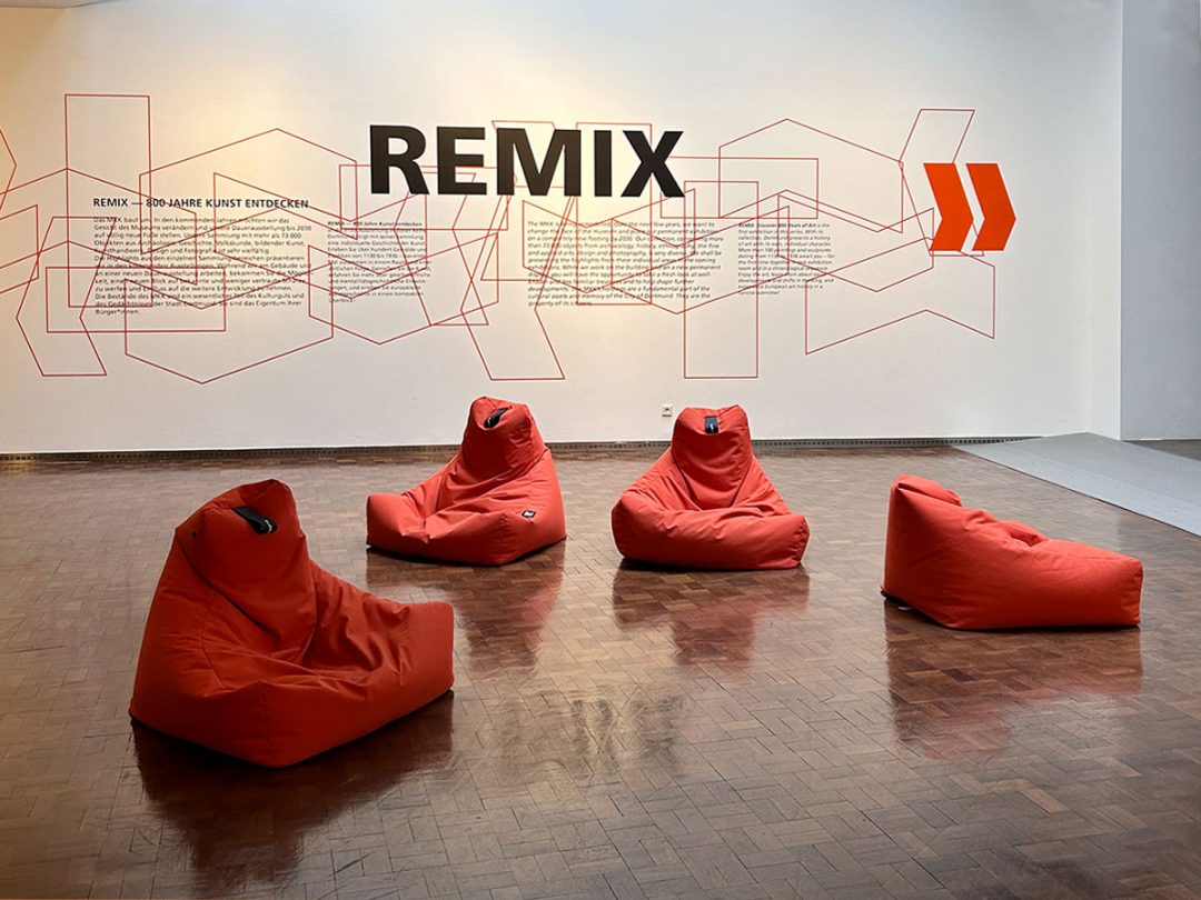 Ein Szene aus einem Museum rote Knautschsessel vor einer Wand mit abstraktem Muster und dem Schriftzug "Remix"